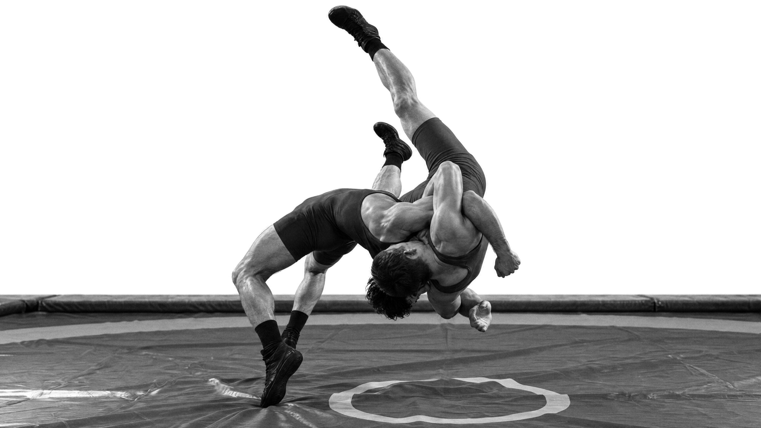 Two wrestlers in a throw on a wrestling mat